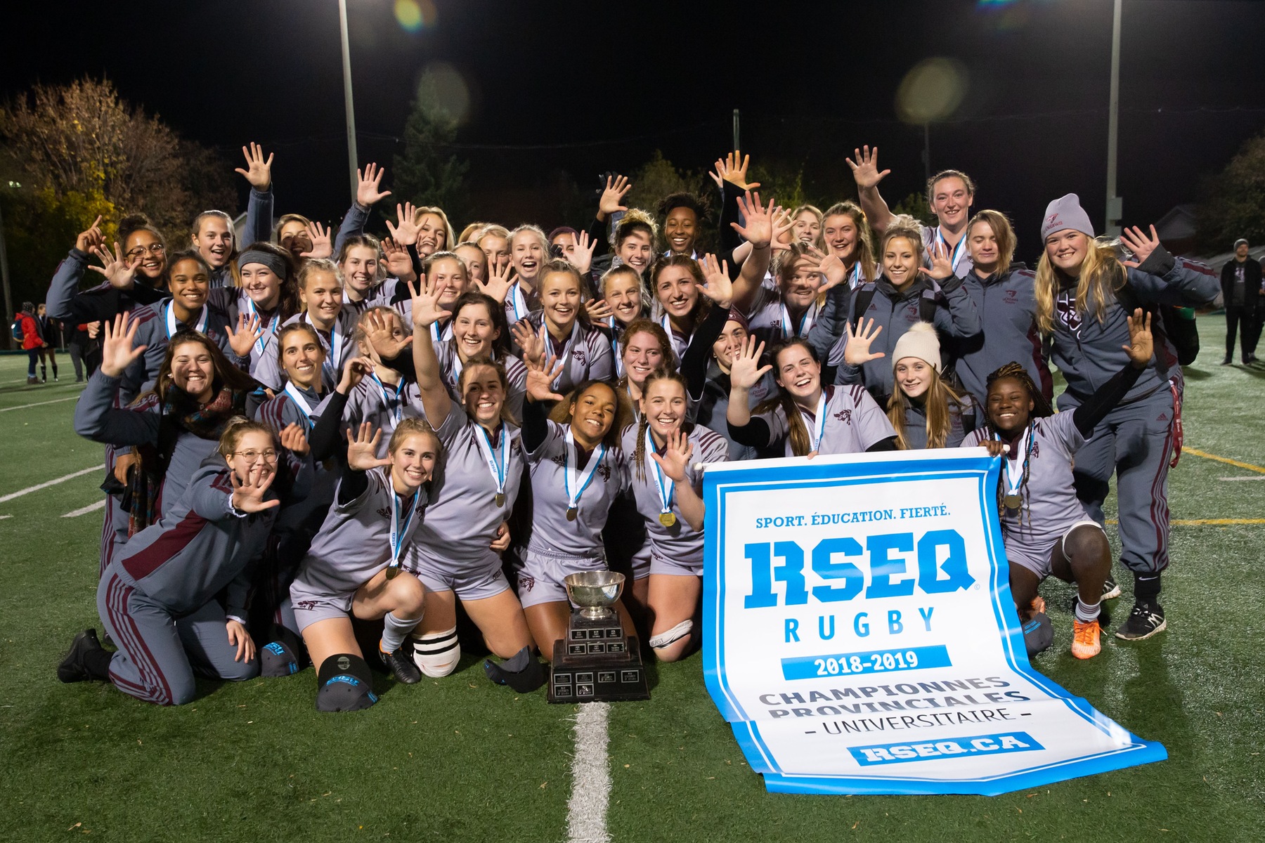 Team holds 2018 RSEQ championship banner at Matt Anthony Field.