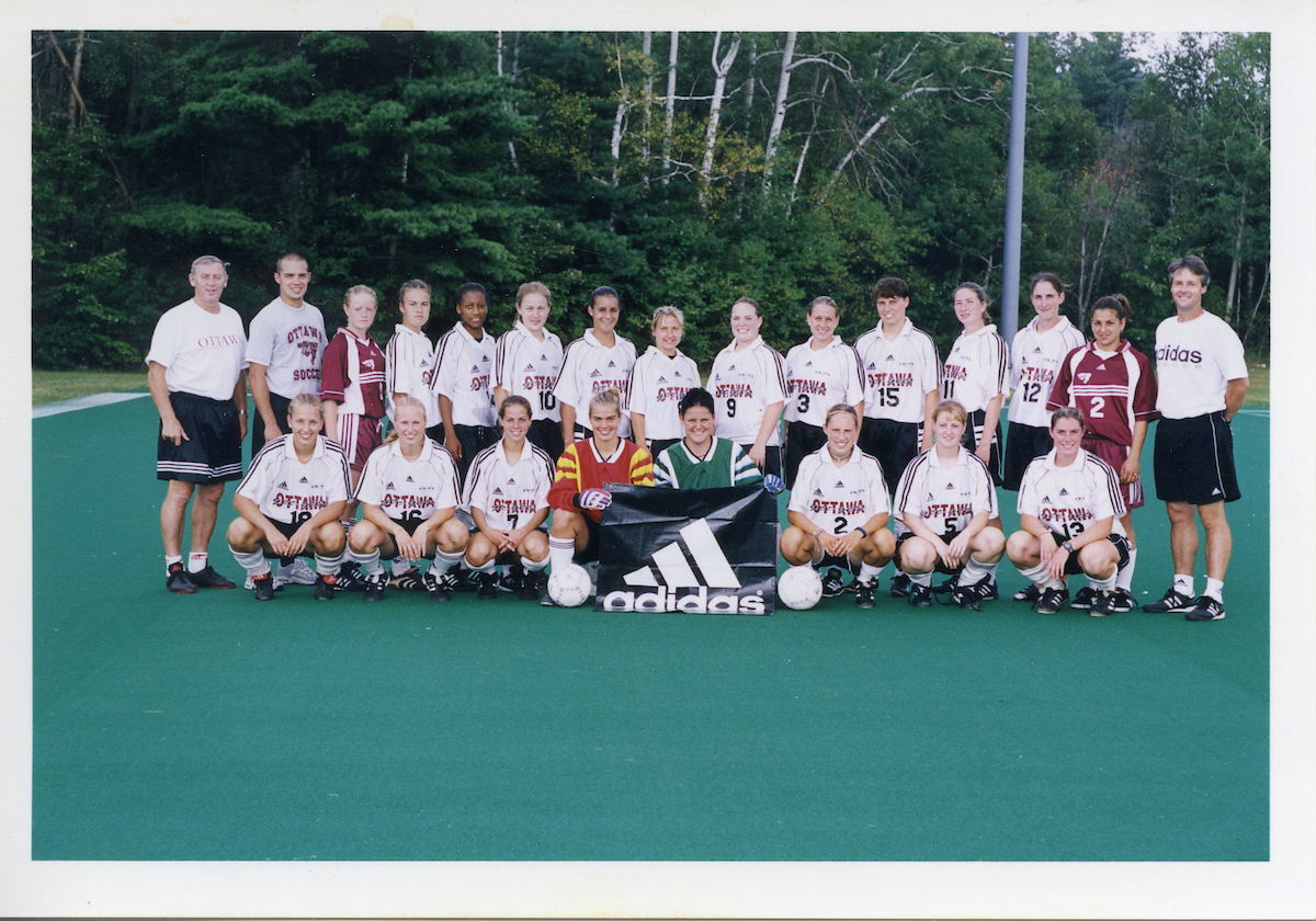 The Gee-Gees women's soccer team from the 2000 season, posing for a team photo while holding an Adidas sponsor sign. 
