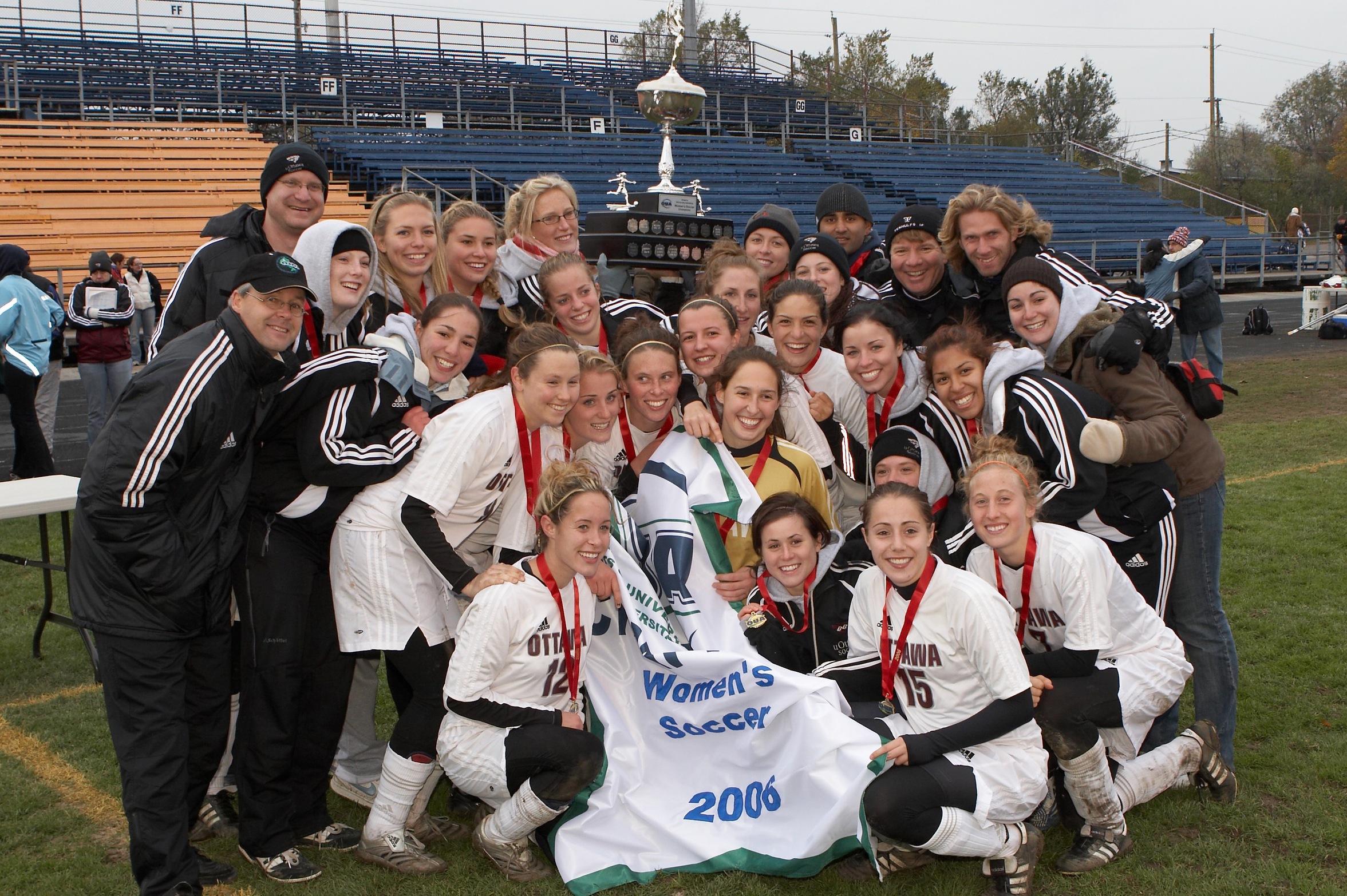 2006 Gee-Gees women's soccer team group photo on the field at Queen's with the OUA Championship banner and trophy.